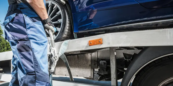 A tow truck driver strapping a blue car down on a flatbed tow truck